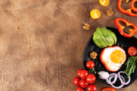 Delicious family breakfast table with fried scrambled egg, avocado, cherry tomatoes, bell peppers, walnut and onion rings on the black pan. Copy space.の写真素材