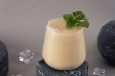 Glass of traditional Indian lassi drink with mint leaf, mango and ice on a grey background.の写真素材