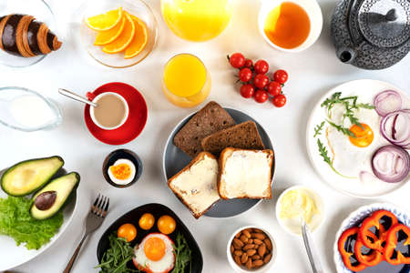 Delicious family breakfast table with coffee, tea, orange juice, croissants, toast, butter, fried and boiled eggs, avocado, cherry tomatoes, almond and salad. Top view.の写真素材