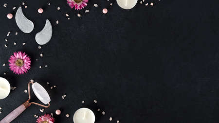 Spa treatments with gouache facial massage roller and eye patches. Trending skin care. Lifting for youthful skin. Organic cosmetics on dark background with pink sea salt. Copy space. Top view.の写真素材