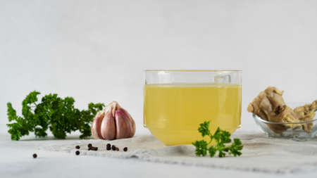 Homemade beef bone broth in glass cup with parsley, peppercorns, garlic, bonesの写真素材