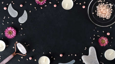 Spa salon with gouache scraper, facial massage roller, eye patches and collagen powder. Skin care. Lifting for youthful skin. Organic cosmetics on dark background with sea salt. Copy space. Top viewの写真素材