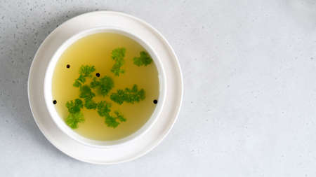 Homemade beef bone broth in white bawl with parsley leaves and peppercorns.の写真素材