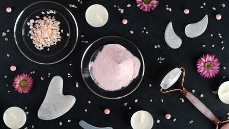 Spa treatments with gouache scraper, facial massage roller, eye patches and collagen powder. Trending skin care. Lifting for youthful skin. Organic cosmetics on dark background with sea salt. Top viewの写真素材