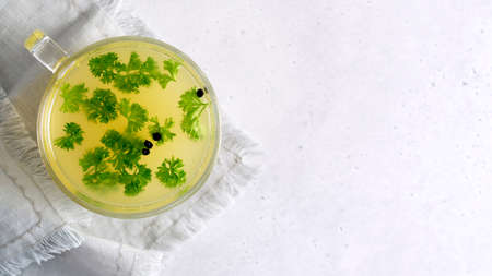 Cup of homemade chicken bone broth with parsley leaves and peppercorns.の写真素材