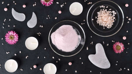 Spa treatments with gouache scraper, eye patches, collagen powder and spa sea salt. Trending skin care. Lifting for youthful skin. Organic cosmetics on dark background with flowers and beads. Top viewの写真素材