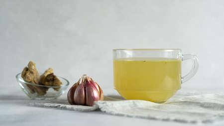 Homemade beef bone broth in glass cup with bulb of garlic and bones in glass bawl.の写真素材