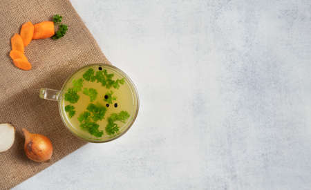 Homemade Beef Bone Broth in glass mug with onion, carrot and parsley leaves.の写真素材