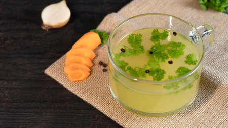Homemade chicken Bone Broth in glass cup with onion, carrot, parsley leaves.の写真素材