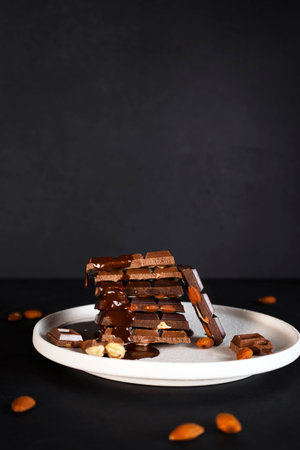 Melted liquid chocolate pours on a plate with pieces of chocolate bars with almond. Vertical...