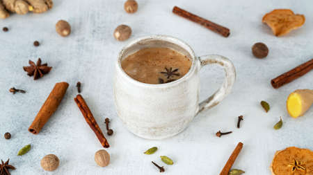 Traditional Indian Masala chai tea in ceramic cup with ingredients: cinnamon, ginger, nutmeg, cardamom, anise, honey, cloves. Spicy black tea with milk.の写真素材
