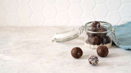 Healthy energy protein balls with nuts, dates, peanut butter, cocoa powder, coconut flakes, oats in glass jar on the kitchen. Homemade truffles. Vegan raw fitness food snack. Side view. Copy space.の写真素材