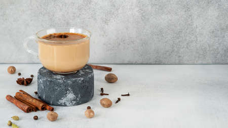 Masala tea chai in a glass cup on podium or pedestal. Traditional Indian drink - spicy black tea with ingredients: cinnamon, ginger, nutmeg, cardamom, anise, honey, cloves and milk. Copy space.の写真素材