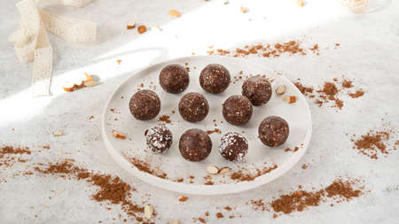 Homemade healthy raw vegetarian dessert energy balls with nuts, dates, peanut butter, cocoa powder, coconut flakes and oats on white plate with sunlight. Healthy eating. Fitness snack. Selective focusの写真素材