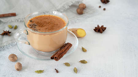 Masala tea chai in a glass cup with ingredients for cooking. Cinnamon sticks, ginger, cardamom, anise, honey, cloves. Traditional Indian drink - spicy black tea with spices and milk.の写真素材