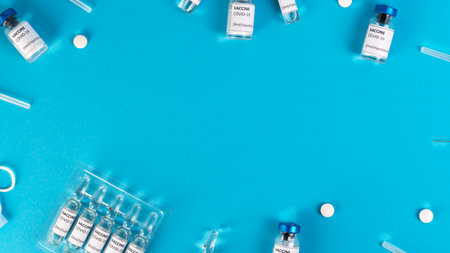 Covid vaccination concept. Coronavirus Covid-19 vaccine vials, ampoules, syringes, protective face masks, pills on a blue medical background. Top view. Copy space.の写真素材