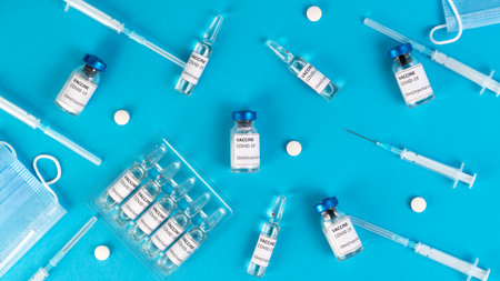 Covid vaccination concept. Coronavirus Covid-19 vaccine vials, ampoules, syringes, protective face masks, pills on a blue medical background. Top view.の写真素材