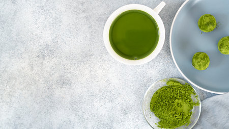 No bake energy balls with a cup of matcha tea. Homemade raw vegan dessert covered by matcha tea powder. Healthy eating. The perfect snack during fitness classes. Selective focus. Top view.の写真素材