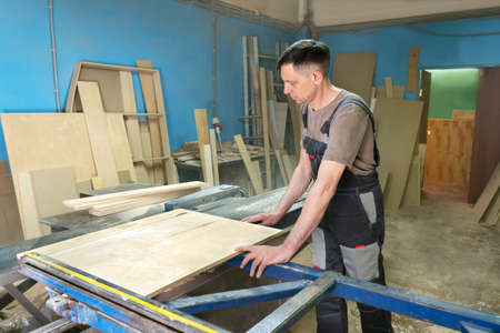 A carpenter cuts wood on a circular saw in a joinery. Furniture manufacture.