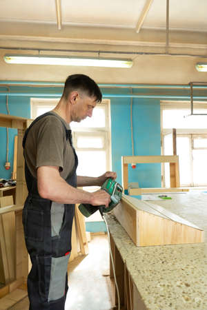 A professional carpenter with a wood grinding machine. Furniture manufacture. Vertical orientation.