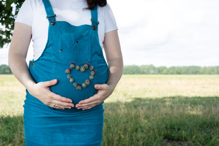 Young pregnant woman in blue sundress with heart shape with flowers. Copy space.