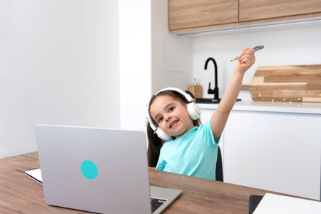 Happy smiling preschooler girl raising hand with pen. Distant online lesson.の写真素材
