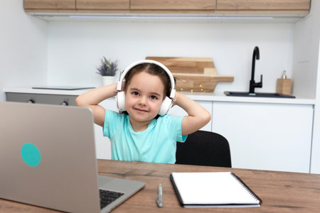 Smiling little girl raising her hands and rejoices at the end of online lessons.の写真素材