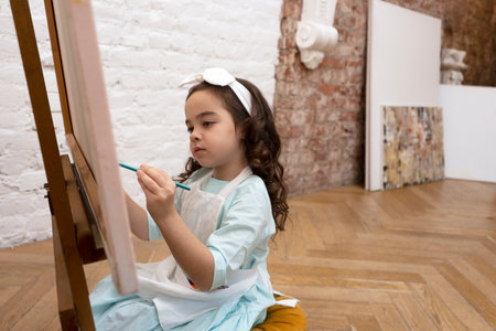 Pretty little artist painting on canvas easel with pencil. Drawing lesson in preschool.の写真素材
