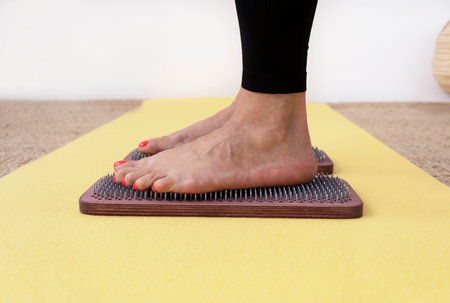 Close-up of womans feet standing on wooden sadhu board with sharp nails on yellow yoga mat.の写真素材