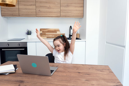 Smiling little girl raising her hands and rejoices at the end of online lessons.