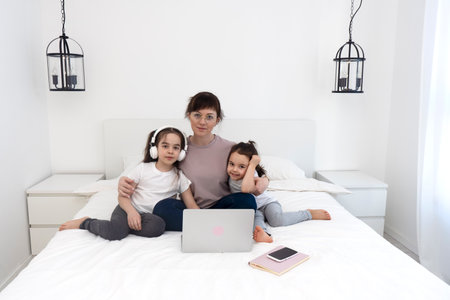 Young mother with two daughters chatting with teacher online. Online lesson.の写真素材