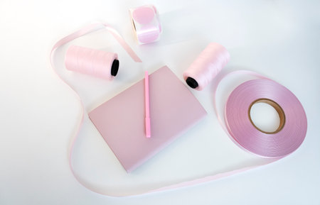 Pink coil of satin ribbon for labels or branding, roll of labels for thermal printing and two spools of thread. Clothing production.の写真素材