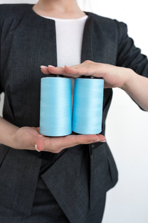 Fashion designer the owner of a small business of sewing production keeps two blue spools of thread in hands.の写真素材