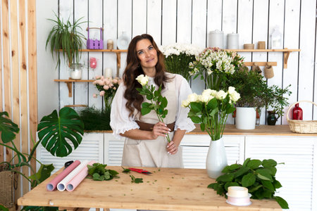 Beautiful smiling female florist in flower shop with bouquet of white roses.の写真素材