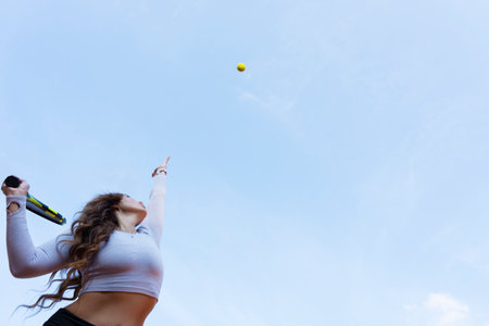Female tennis player wearing crop top and skirt playing tennis on the tennis court. Copy space. Blue sky background.の写真素材