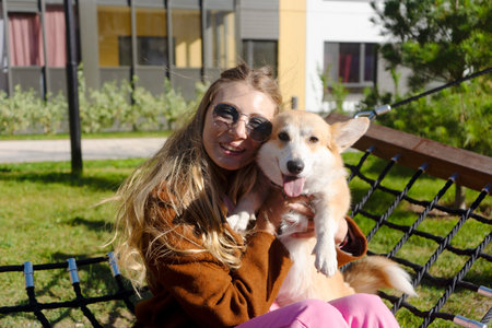 Portrait of two best friends. Happy girl in sunglasses and her corgi dog puppy swing on a hammock and enjoy the sunny weather. Lovely pets.の写真素材
