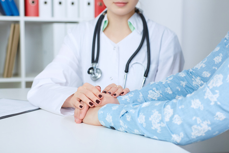 Young female doctor holding patient's hand for encouragement and empathy. Partnership, trust and medical ethics concept. Bad news lessening and support. Patient's cheering.の写真素材