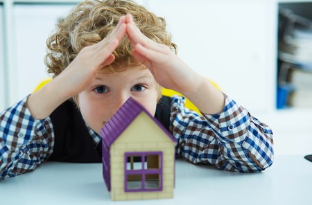 Little curly caucasian boy folded his hands in the form of a roof over a figurine at house.の写真素材