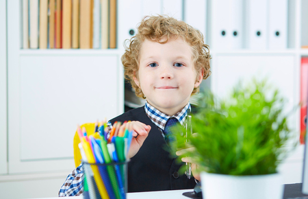 Little schoolboy in the form of an office worker plays with the dividers. Smiling boy looking at the camera.の写真素材