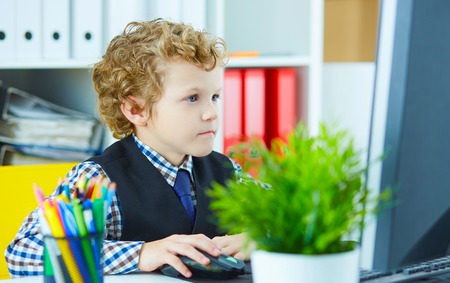 Little caucasian schoolboy plays in boss, working at computer.の写真素材