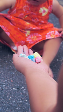 Mom gives the girl crayons for drawing on the asphaltの写真素材