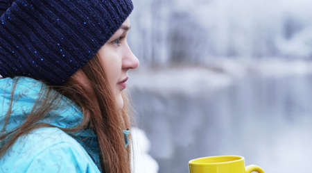 Close up portrait of a beautiful girl dreaming looking into the distance standing outdoor with cup of tea.の写真素材