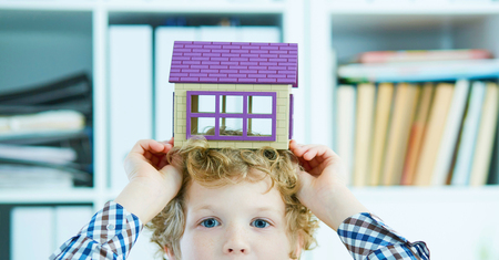 Little Caucasian curly boy holding the plastic figure of houseover his head close-up. Family home security concept.の写真素材