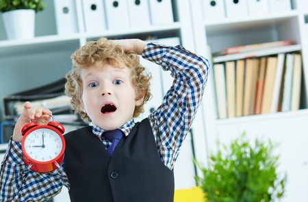 Disappointed kid boss holding a big red alarm clock in his hand suggesting you are late for work. Work, responsibility, success, timemanagement concept.の写真素材