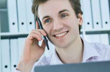 Business man talking on smart phone and look to laptop screen, male freelancer working on computer.の写真素材