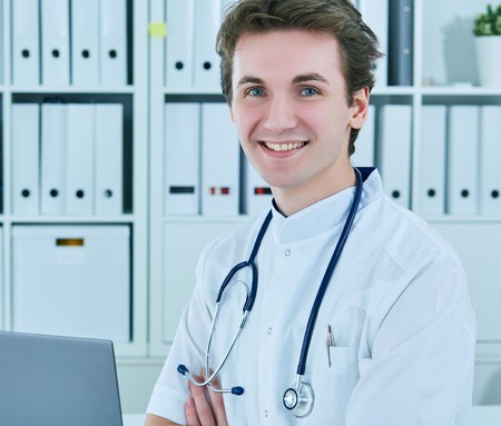 Portrait of smiling doctor sitting with his hands crossed. Young doctors, confidence, trust, openness.の写真素材