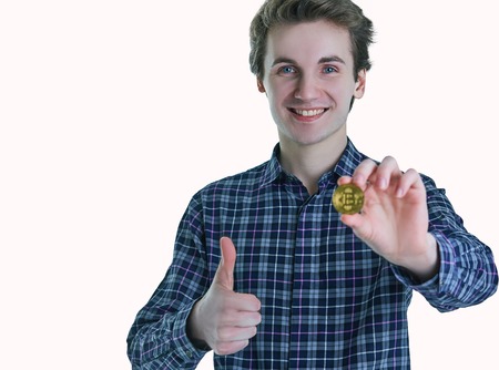 Boy in blue shirt holds bitcoin and shows raised thumb. Isolated on white background. Concept of bitcoin as the currency of the new generation.の写真素材