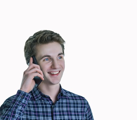 Cheerful young man speaking on the phone on white background. Pleasant conversation, conversation with a loved one, good news.の写真素材