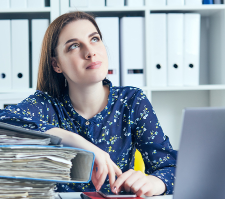 Business woman or secretary with many documents folders bills on her desk taking break, relaxing at work thinking day dreaming.の写真素材