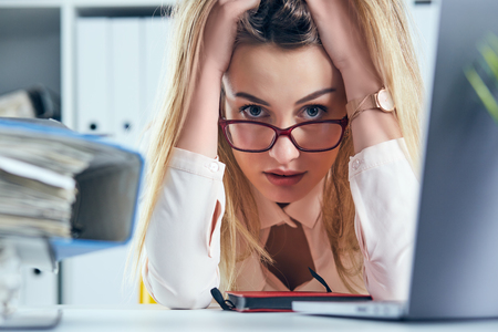Tired and exhausted woman in spectacles looks at the camera near the mountain of documents propping up her head with her hands.の写真素材